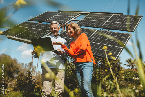 Happy mature couple discussing over laptop in front of solar panels photo