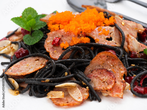 Plate of black spaghetti squid ink with spicy bacon and shrimp roe cream isolated on white background. Close up