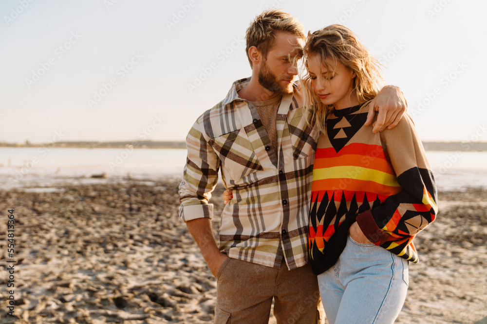 Happy young white couple hugging and walking by seashore Happy young white couple hugging and walking by seashore
