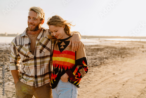 Happy young white couple hugging and walking by seashore