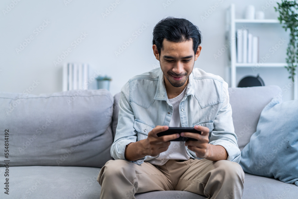 Asian young handsome man gamer play mobile game on smartphone at home. 