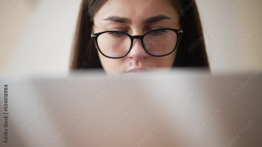 Close-up view of laptop cover and tired eyes of young woman wearing glasses. Portrait of tired woman who working in home freelance office and looks at screen intently. Sadness on hard day at work. Close-up view of laptop cover and tired eyes of young woman wearing glasses. Portrait of tired woman who working in home freelance office and looks at screen intently. Sadness on hard day at work.
