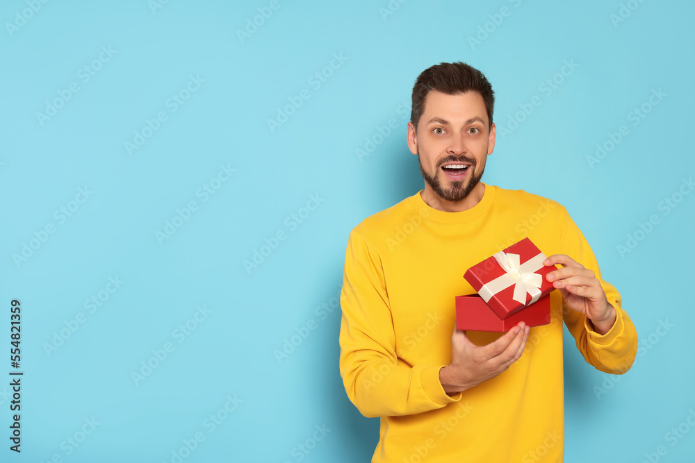 Happy man with gift box on light blue background, space for text