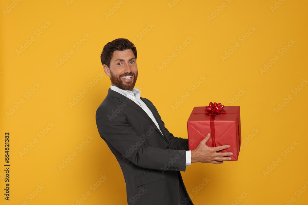 Handsome man holding gift box on yellow background Handsome man holding gift box on yellow background