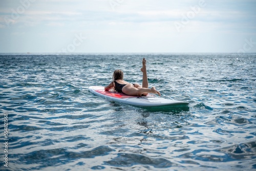Woman sap sea. Sports girl on a surfboard in the sea on a sunny summer day. In a black bathing suit, he lies on a sap in the sea. Rest on the sea.