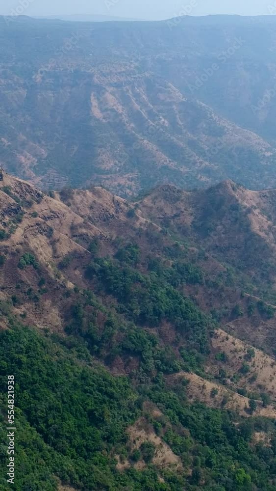 Vertical aerial video of valley between hills with steep rocky cliffs around