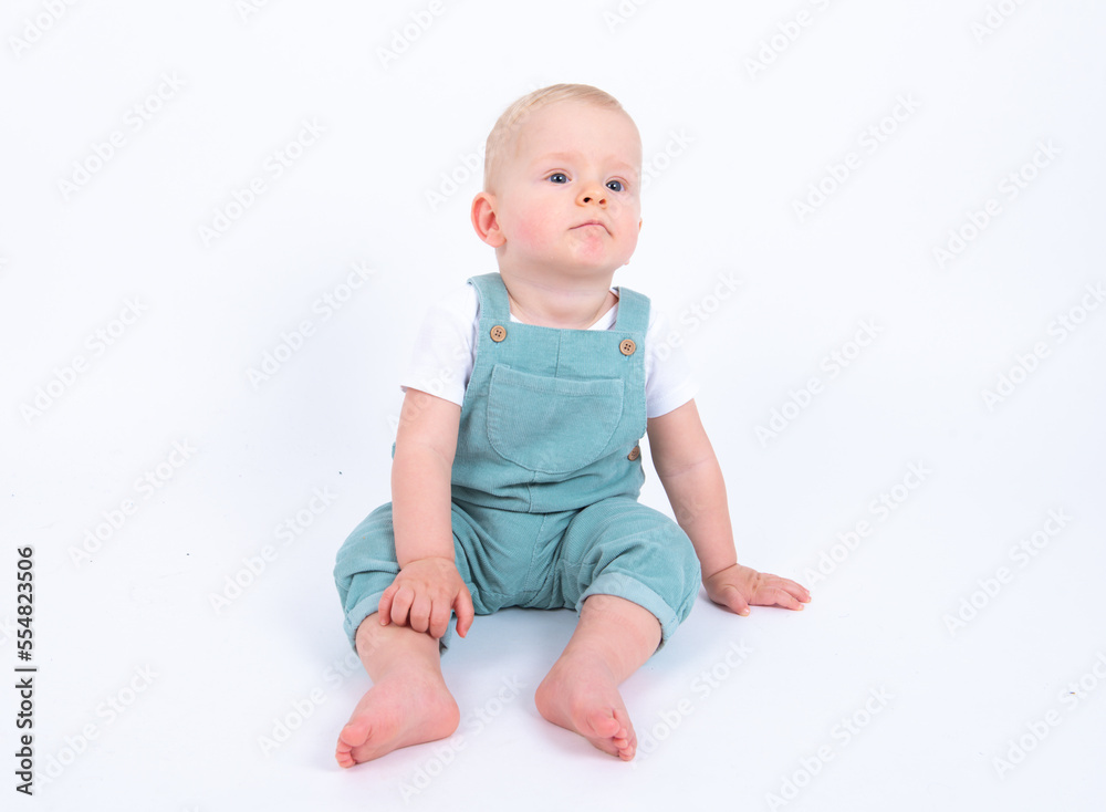 Close-up portrait of beautiful baby boy wearing light blue jumpsuit over white studio background smiling and looking aside. Close-up portrait of beautiful baby boy wearing light blue jumpsuit over white studio background smiling and looking aside.