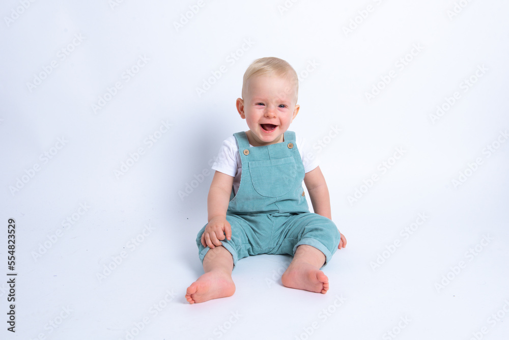 Close-up portrait of beautiful baby boy wearing light blue jumpsuit over white studio background smiling and looking to the camera. Close-up portrait of beautiful baby boy wearing light blue jumpsuit over white studio background smiling and looking to the camera.