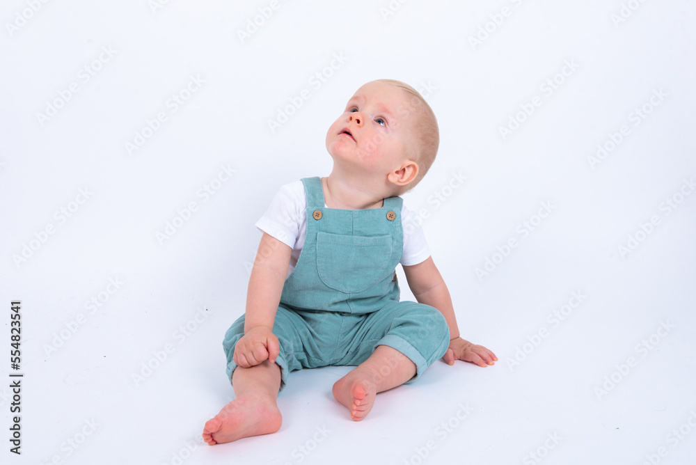 Close-up portrait of beautiful baby boy wearing light blue jumpsuit over white studio background smiling and looking aside. 