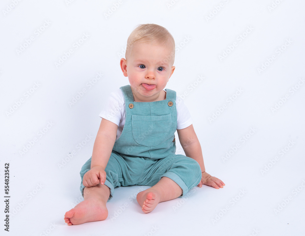 Portrait of beautiful baby boy wearing light blue jumpsuit over white studio background showing his tongue, smiling and looking to the camera. Portrait of beautiful baby boy wearing light blue jumpsuit over white studio background showing his tongue, smiling and looking to the camera.