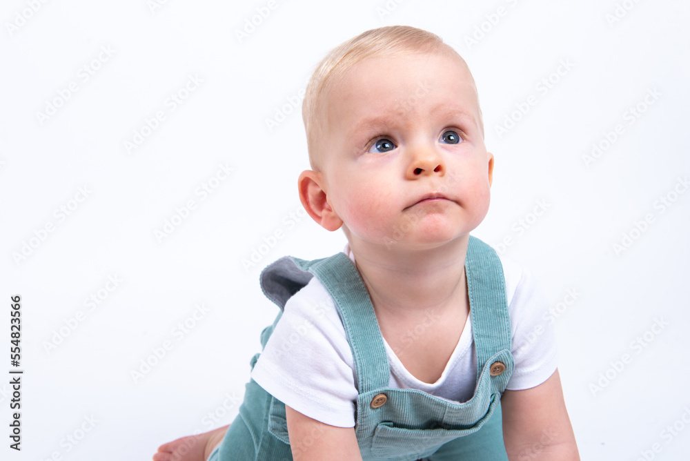 Close-up portrait of beautiful baby boy wearing light blue jumpsuit over white studio background looking up. Close-up portrait of beautiful baby boy wearing light blue jumpsuit over white studio background looking up.