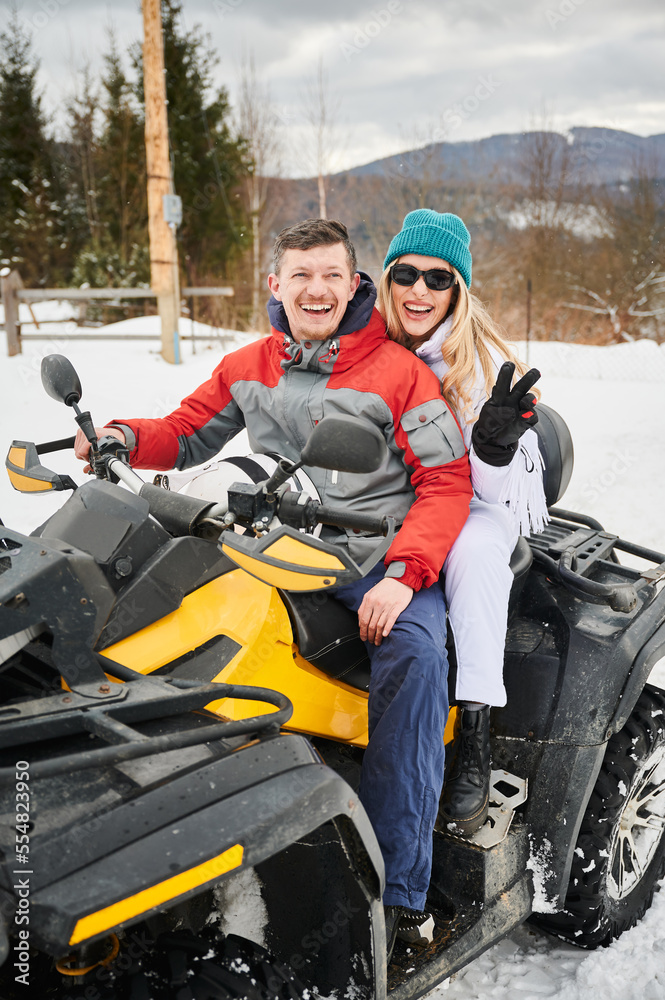 Portrait of happy man and woman posing on offroad four-wheeler ATV. Concept of active leisure and winter activities.