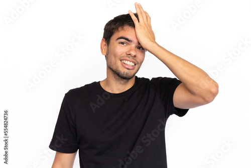 Frustrated young man with hand on forehead. Regretful Caucasian male model with short dark hair in black T-shirt looking at camera, smiling, realizing mistake or forgetting something. Regret concept