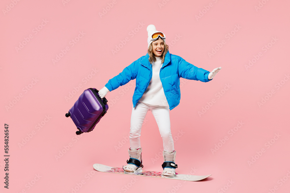 Snowboarder woman in blue suit goggles mask hat ski jacket hold bag snowboarding isolated on plain pink background Tourist travel abroad in free spare time rest. Air flight winter trip sport concept