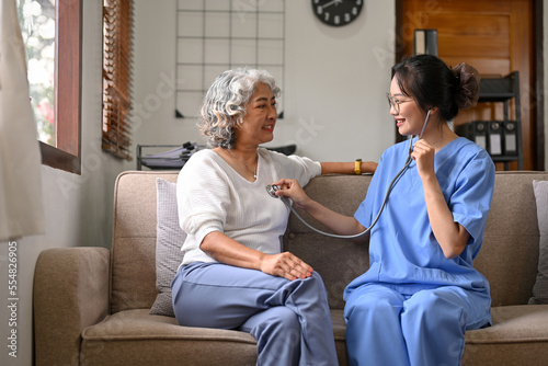 Professional Asian female doctor hold stethoscope listen to elderly female patient's heart rate