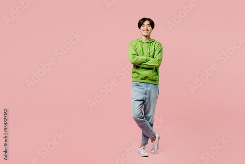 Full body smiling happy fun young man of Asian ethnicity wear green hoody look camera hold hands crossed folded isolated on plain pastel light pink background studio portrait People lifestyle concept