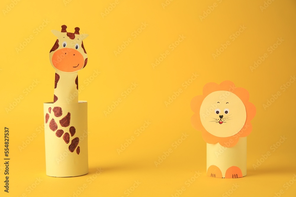 Fototapeta premium Toy giraffe and lion made from toilet paper hubs on yellow background, space for text. Children's handmade ideas