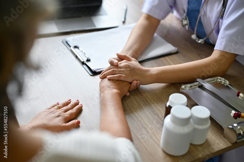 A female doctor holding her patient's hands on the table while discussing the treatment plan.