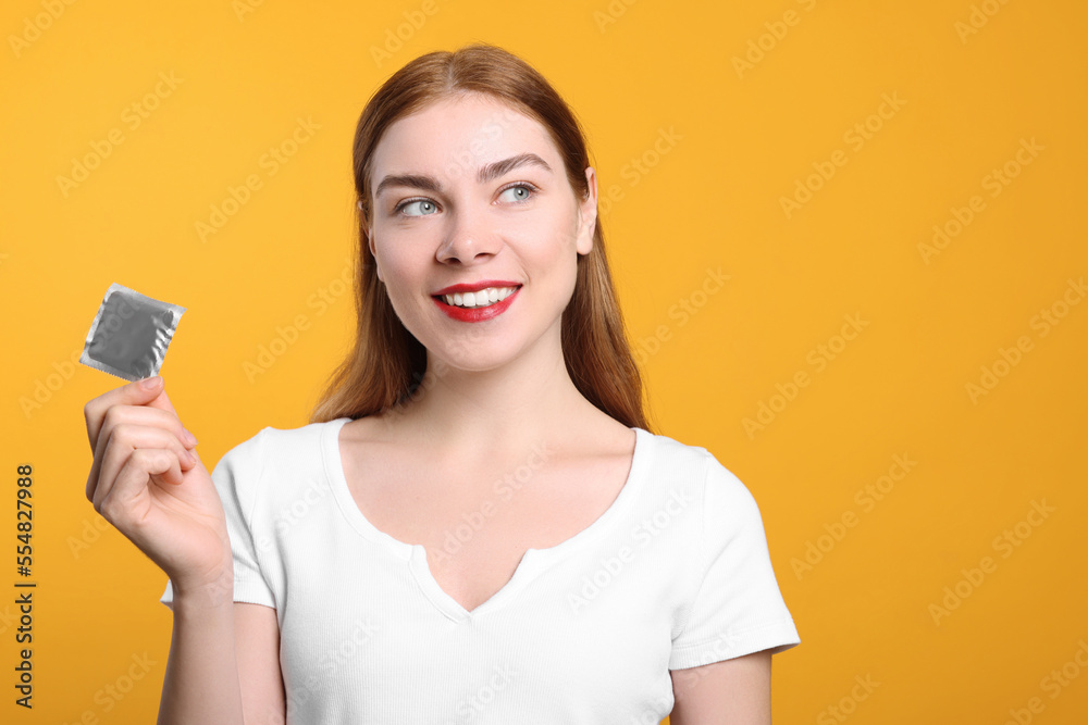 Woman holding condom on yellow background, space for text. Safe sex Woman holding condom on yellow background, space for text. Safe sex