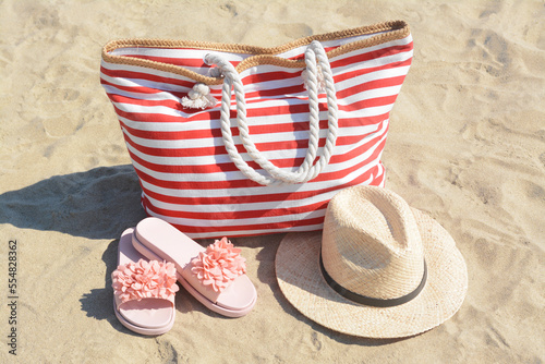 Fototapeta Naklejka Na Ścianę i Meble -  Stylish striped bag with straw hat and slippers on sandy beach