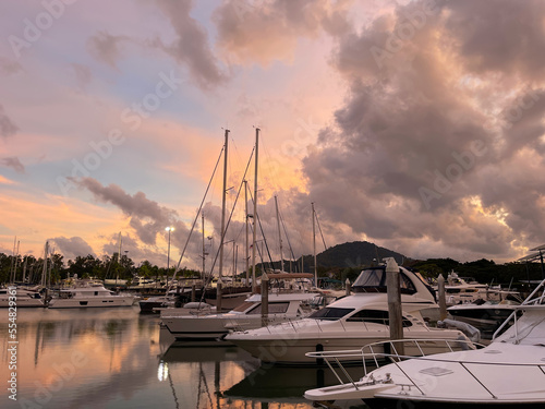 Beautiful sunset at Phuket Boat Lagoon. Amazing sky with clouds and bright setting sun glow. Smooth surface of water. Yacht club. Amazing Thailand. Luxury yachts, sailboat, boats moored in sea harbor.