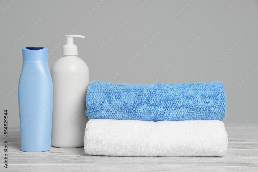 Soft folded towels with cosmetic products on white wooden table against light grey background Soft folded towels with cosmetic products on white wooden table against light grey background