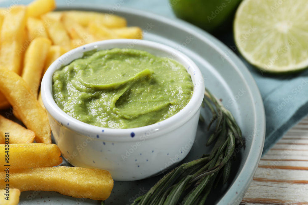Plate with delicious french fries, avocado dip, lime and rosemary served on white wooden table, closeup Plate with delicious french fries, avocado dip, lime and rosemary served on white wooden table, closeup