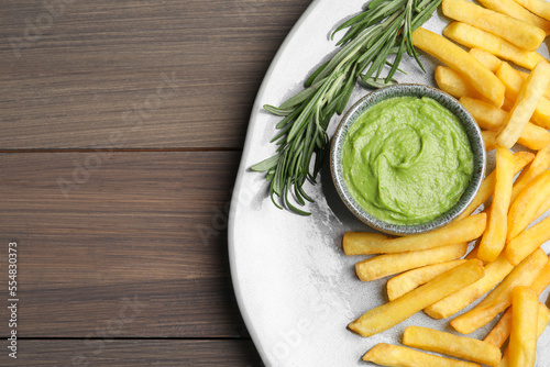 Plate with delicious french fries, avocado dip and rosemary served on wooden table, top view. Space for text