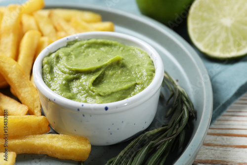 Plate with delicious french fries, avocado dip, lime and rosemary served on white wooden table, closeup