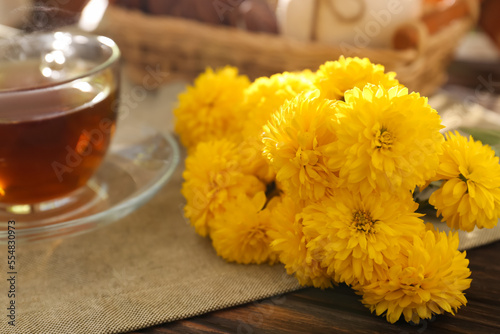 Beautiful yellow chrysanthemum flowers and cup of aromatic tea on wooden table, closeup