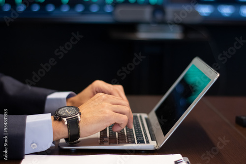 Side view of male hands on laptop keyboard. Professional trader typing on computer in office monitoring financial data on stock market exchange. Financial analytics and business strategy concept