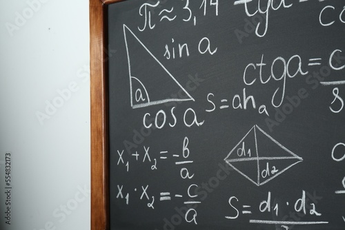 Chalkboard with many different math formulas on white wall, closeup