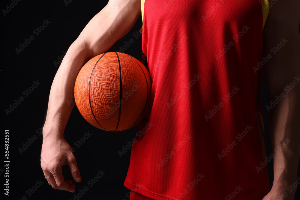 Athletic man with basketball ball on black background, closeup