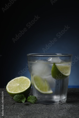 Glass of vodka with lime slices, mint and ice on grey table