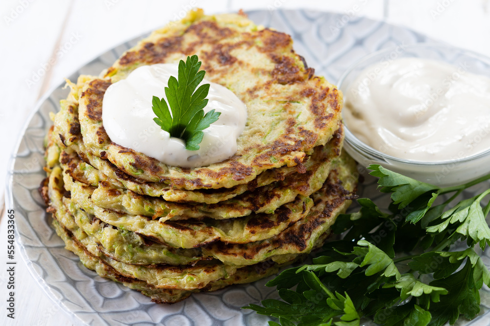 Zucchini fritters with yogurt sauce on white wooden table Zucchini fritters with yogurt sauce on white wooden table