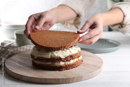 Bilde på lerret Woman stacking layers of sponge cake at white wooden table, closeup