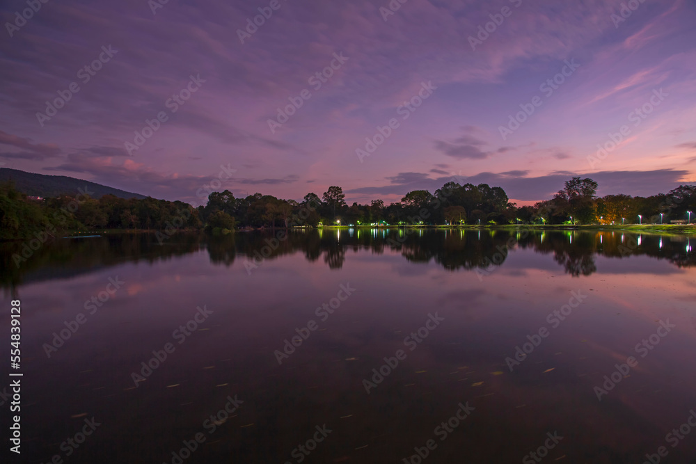 The cloud and trees on water reflection in the beautiful sunrise at Ang Kaew of Chiangmai University, and there is a relaxing break for exercisers and tourists