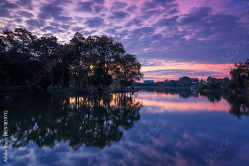 The cloud and trees on water reflection in the beautiful sunrise at Ang Kaew of Chiangmai University, and there is a relaxing break for exercisers and tourists