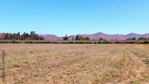 Panoramic view of an agricultural drone performing a trajectory in a dry straw field, mountainous background. photo