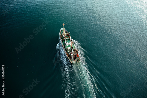 Fishing boat catching fish aerial top view from drone. Small fishing trawler ship on sea surface.