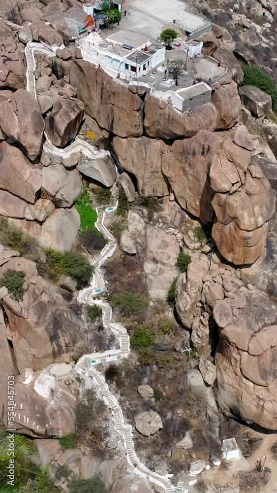 Vertical video of Aerial shot of rocky boulder hill with white temple on top, fields at bottom Vertical video of Aerial shot of rocky boulder hill with white temple on top, fields at bottom