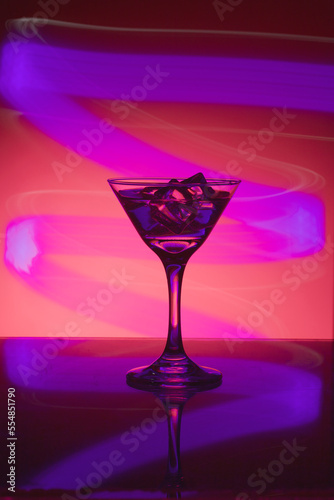 Martini glass with ice. On the bar. Against the background of neon light.