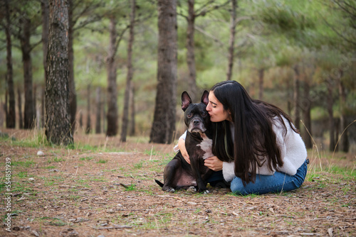 Young caucasian woman kissing her mixed breed dog at a pine forest.
