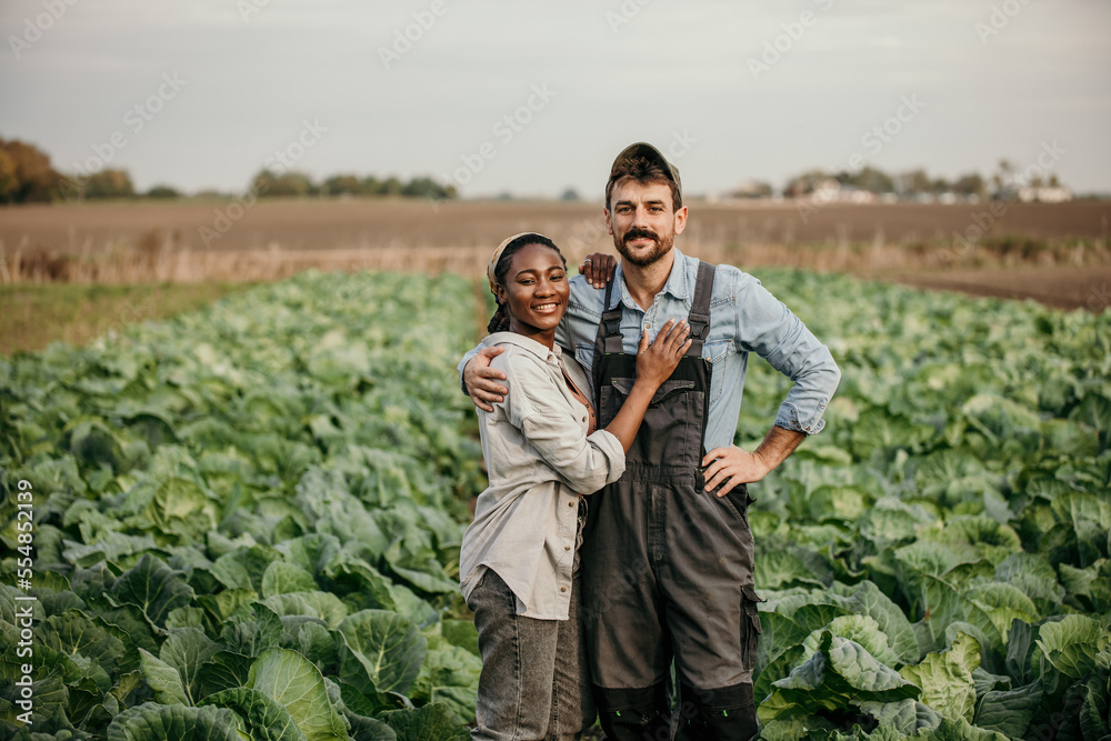 Portrait of a smiling multiracial couple standing in a working outfit in the field, small family business concept