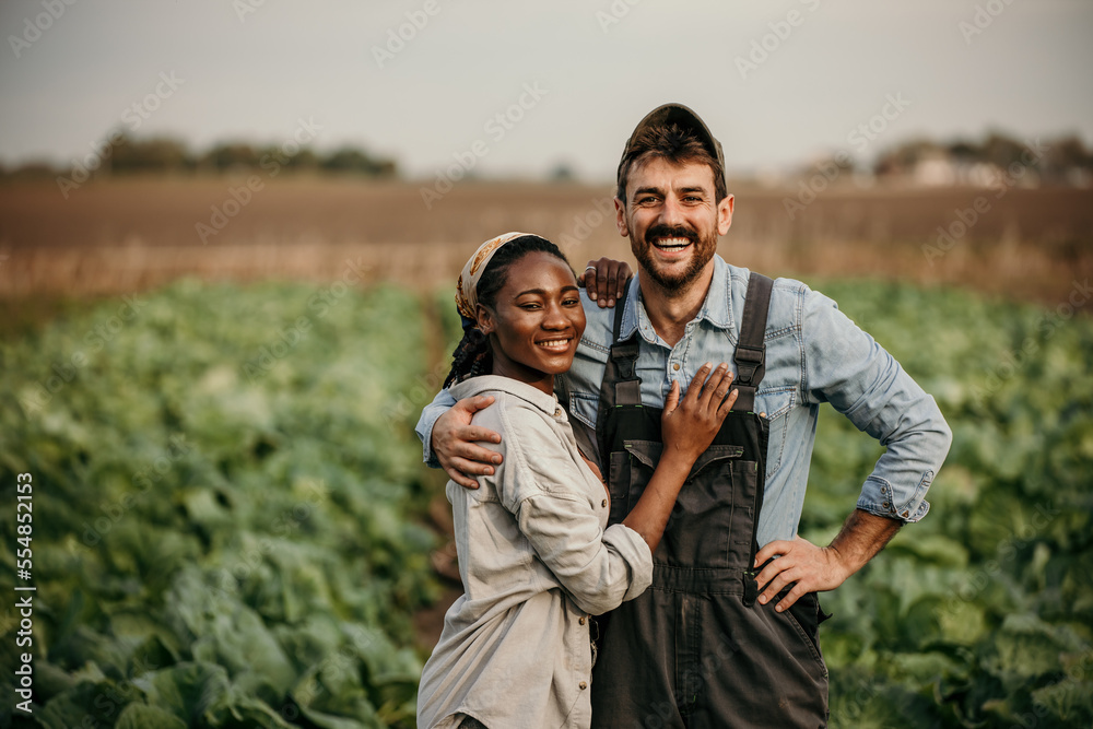 Portrait of a smiling multiracial couple standing in a working outfit in the field, small family business concept Portrait of a smiling multiracial couple standing in a working outfit in the field, small family business concept