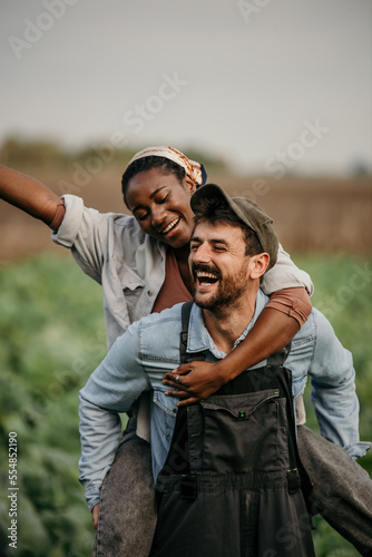 Man and woman field workes having fun and a piggyback ride during a workday on the farm. © La Famiglia
