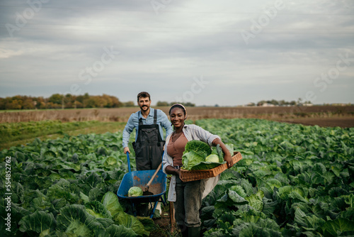 Shot of an attractive young female and male farmers in working clothes carrying a crate of fresh produce.
