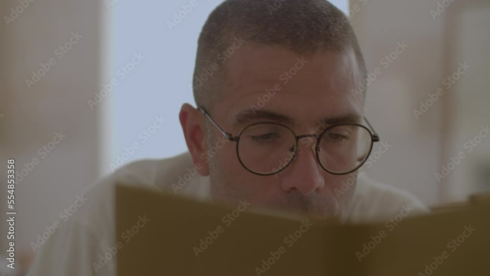 Focused Caucasian man reading book in bed after waking up. Close-up shot of handsome man in eyeglasses lying in bed, relaxing on weekend, preparing for start of new day. Dream, development concept Focused Caucasian man reading book in bed after waking up. Close-up shot of handsome man in eyeglasses lying in bed, relaxing on weekend, preparing for start of new day. Dream, development concept