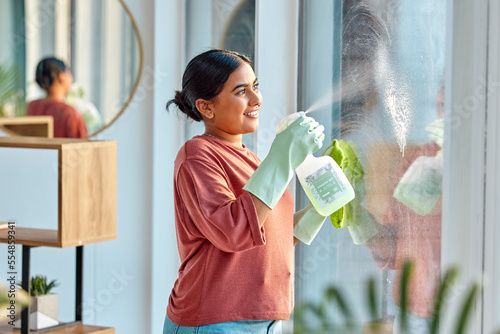 Woman, cleaning and spray product of a cleaner washing a window with a smile in home. Happy working maid use a home hygiene bottle and cloth to disinfect the house furniture with a sanitizer bottle