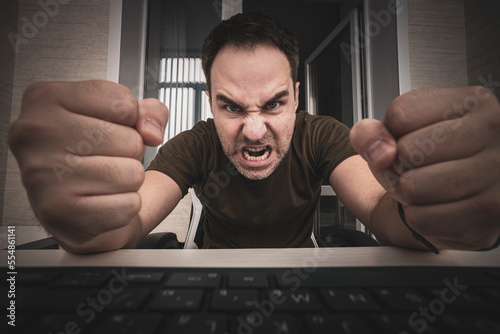 freelancer punches the keyboard. angry man swearing and cursing against information technology and his compuiter worries and hassles - concept of hating computers photo